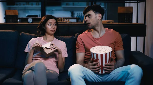 Couple choqué avec de savoureux plats à emporter en se regardant dans le salon — Photo de stock