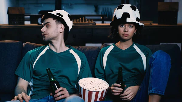 Aficionados al fútbol disgustados en sombreros de abanico sosteniendo botellas de cerveza y viendo el campeonato en la sala de estar - foto de stock