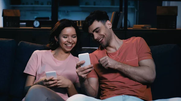 Мужчина и женщина смотрят на мобильный телефон и улыбаются в современной гостиной — стоковое фото