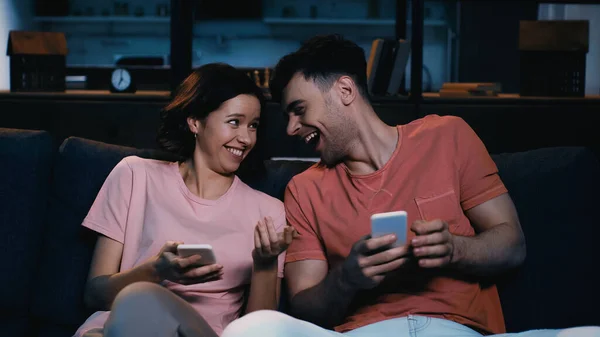 Мужчина и женщина смотрят друг на друга, держа в руках мобильные телефоны в современной гостиной — стоковое фото