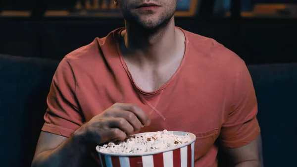 Обрезанный вид человека, держащего ведро попкорна во время просмотра фильма дома — стоковое фото