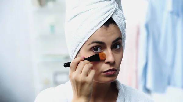 Retrato de jovem mulher com cabeça envolta em toalha aplicando fundação no rosto no quarto — Fotografia de Stock