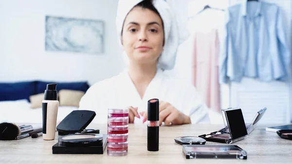 Smiling young woman in bathrobe sitting near table with decorative cosmetics in bedroom — Stock Photo