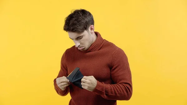 Hombre triste mirando la billetera aislada en amarillo - foto de stock