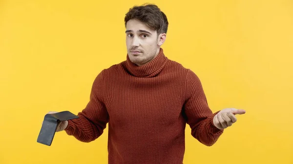 Uomo confuso in maglione che tiene il portafoglio isolato sul giallo — Foto stock