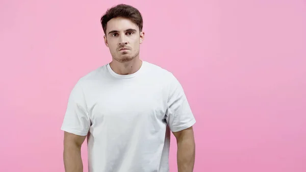 Злой мужчина в белой футболке смотрит на камеру, изолированную на розовый — стоковое фото