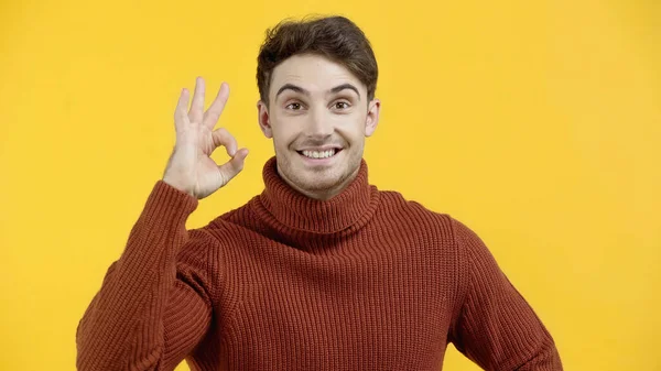 Smiling man in sweater showing okay gesture isolated on yellow — Stock Photo