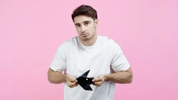 Displeased man showing empty wallet isolated on pink — Stock Photo