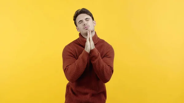 Man in sweater standing with closed eyes and praying hands isolated on yellow — Stock Photo