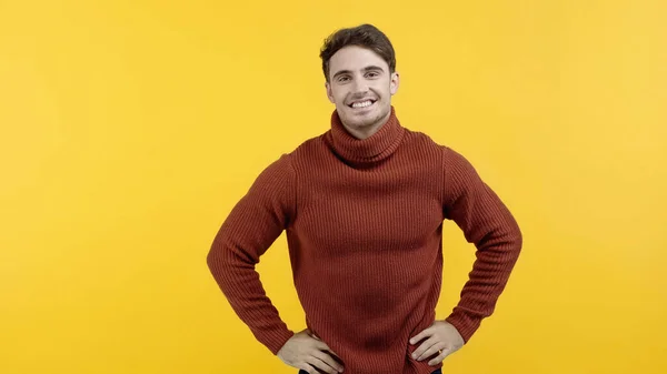 Cheerful man in sweater holding hands on hips isolated on yellow — Stock Photo