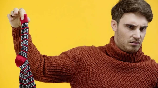 Confused man holding dirty sock isolated on yellow — Stock Photo