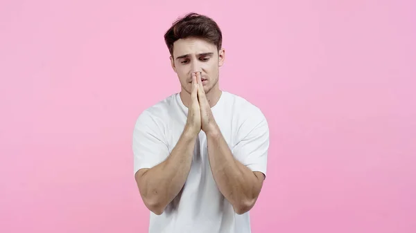 Upset man showing praying hands isolated on pink — Stock Photo