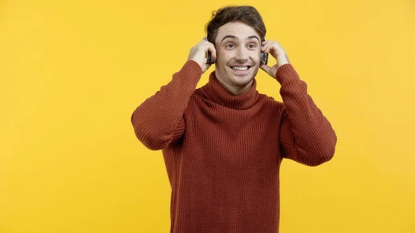 Homme en pull utilisant des écouteurs isolés sur jaune — Photo de stock
