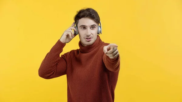 Homem de camisola e fones de ouvido apontando com o dedo isolado no amarelo — Fotografia de Stock