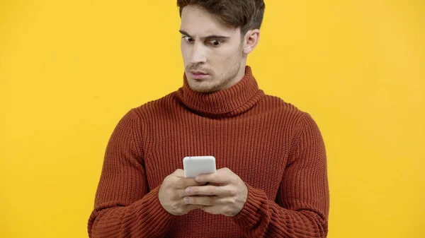 Hombre preocupado en suéter usando teléfono inteligente aislado en amarillo - foto de stock