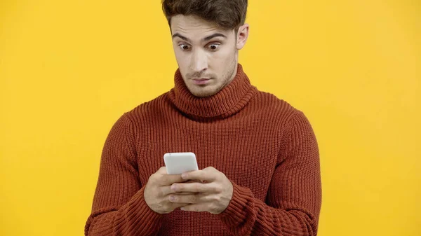 Amazed man in sweater using cellphone isolated on yellow — Stock Photo