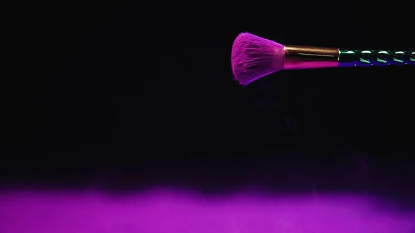 Cosmetic brush with purple holi paint on black background — Stock Photo