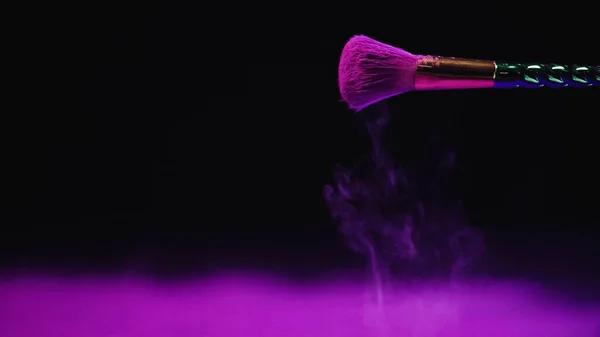 Cosmetic brush with purple powder falling down on black background — Stock Photo