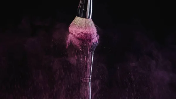 Cosmetic brushes hitting and making splashes of colorful purple holi paint on black background — Stock Photo