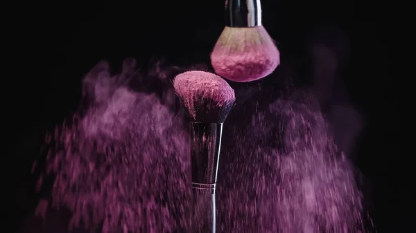 Kosmetikpinsel, die Spritzer lila Holi-Farbe auf schwarzem Hintergrund herstellen — Stockfoto