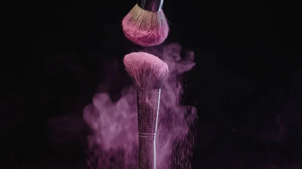 Pennelli cosmetici morbidi che fanno schizzi di vernice rosa holi su sfondo nero — Foto stock