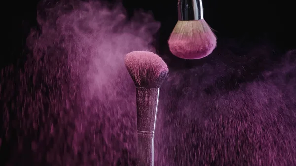 Pinceaux cosmétiques doux près des éclaboussures de peinture holi rose sur fond noir — Photo de stock