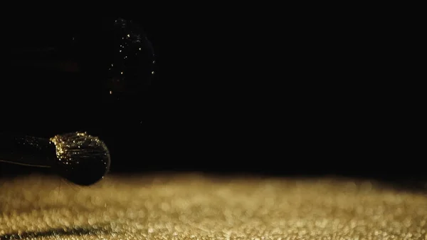 Pinceaux cosmétiques près de poussière dorée brillante sur fond noir — Photo de stock