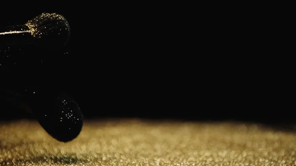 Spazzole cosmetiche vicino lucido polvere dorata su sfondo nero — Foto stock