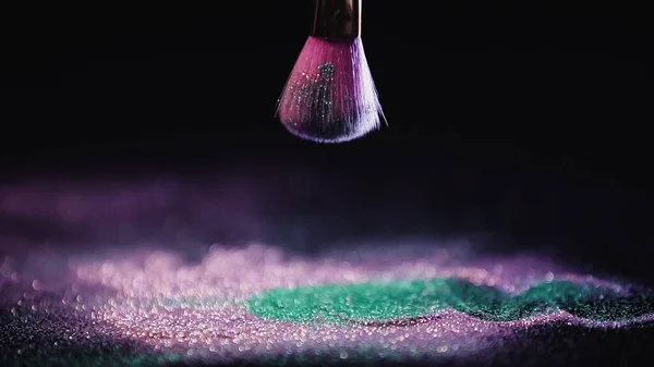 Brosse cosmétique au-dessus de la poussière rose brillant et turquoise sur fond noir — Photo de stock