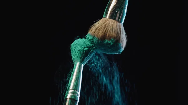 Cosmetic brushes hitting and making splashes of blue holi paint on black background — Stock Photo