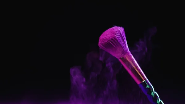 Cepillo cosmético con polvo púrpura cerca del polvo que cae sobre fondo negro - foto de stock