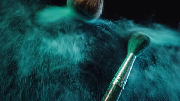 Soft cosmetic brushes making splashes of turquoise dust on black background — Stock Photo