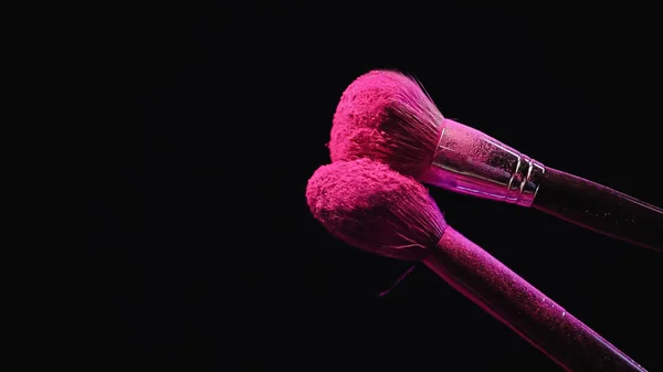 Soft cosmetic brushes with bright pink powder on black background — Stock Photo