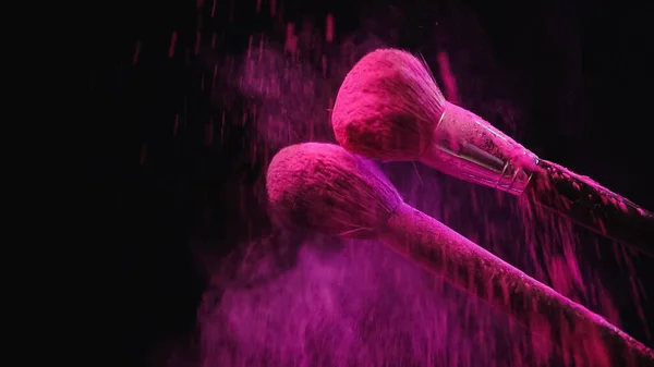 М'які косметичні пензлі, що роблять вибух рожевого порошку на чорному тлі — стокове фото