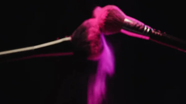 Blurred cosmetic brushes making explosion of pink powder on black background — Stock Photo