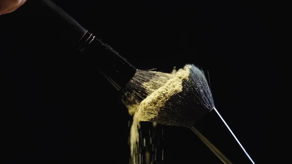 Cosmetic brushes with yellow powder hitting on black background — Stock Photo