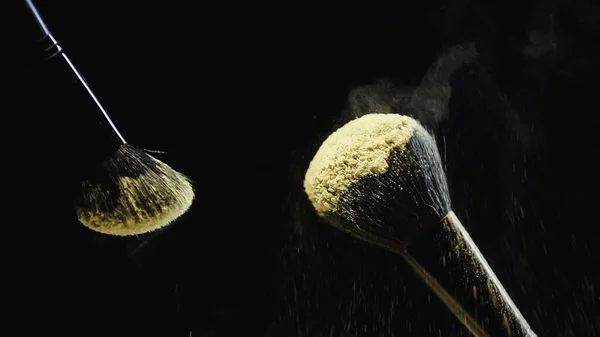 Cosmetic brushes with yellow holi powder on black background — Stock Photo