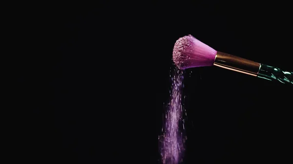 Sparkling pink glitter falling down from soft cosmetic brush on black — Stock Photo