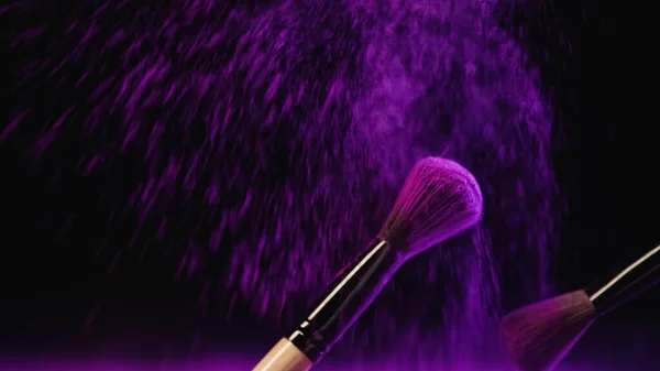 Kosmetikpinsel mit lila Holi-Puder in der Nähe von Staubspritzern auf schwarzem Hintergrund — Stockfoto