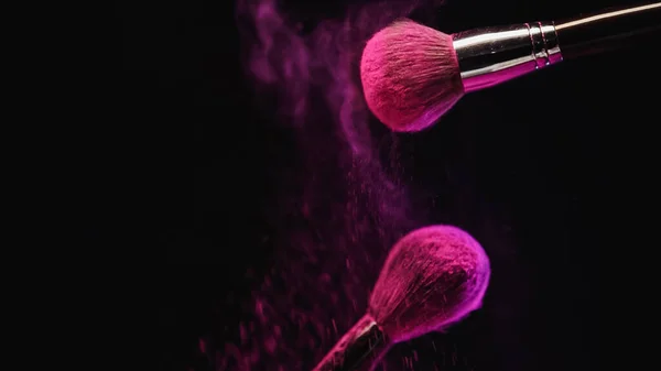 Kosmetikpinsel mit leuchtend rosa Holi-Puder in der Nähe von Staubspritzern auf schwarzem Hintergrund — Stockfoto
