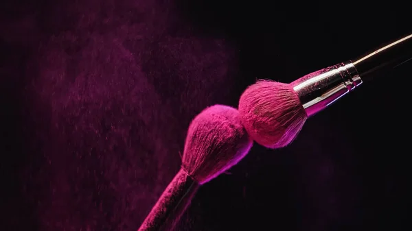 Cosmetic brushes with bright pink powder on black background — Stock Photo