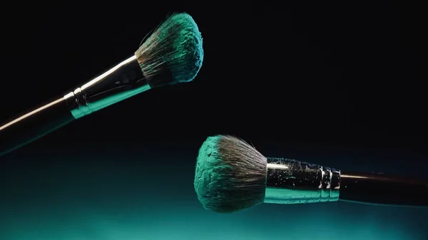 Pinceaux cosmétiques à la poudre turquoise brillante sur fond noir — Photo de stock