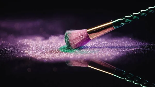 Cosmetic brush near shiny pink and turquoise dust on black background — Stock Photo