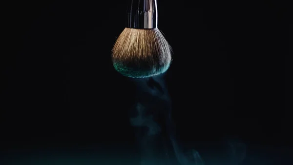 Blue dust falling down from soft cosmetic brush on black — Stock Photo
