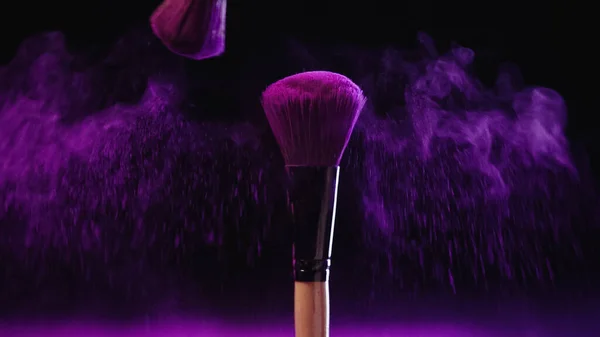 Weiche Kosmetikpinsel mit Holi-Farbe in der Nähe von rosa Staubspritzern auf schwarzem Hintergrund — Stockfoto