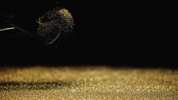 Ігристий золотий пил біля косметичних пензлів на чорному тлі — стокове фото
