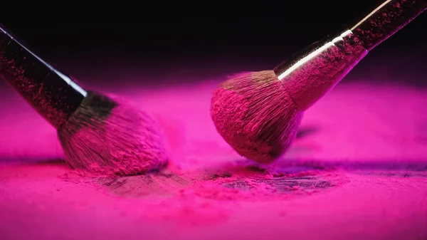 Cepillos cosméticos desordenados cerca de polvo rosa brillante sobre fondo negro - foto de stock