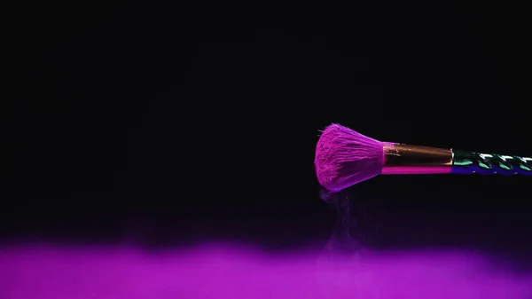 Soft cosmetic brush with vibrant purple powder near dust on black — Stock Photo