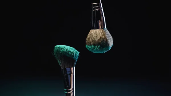 Soft cosmetic brushes with blue holi paint on black background — Stock Photo