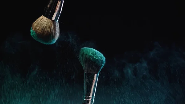Turquoise dust near cosmetic brushes with holi paint on black background — Stock Photo